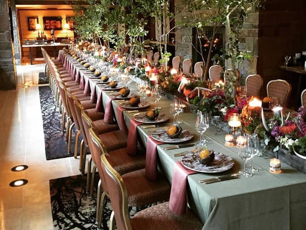 Long wedding banquet table set with fall coloured flowers, small potted trees 