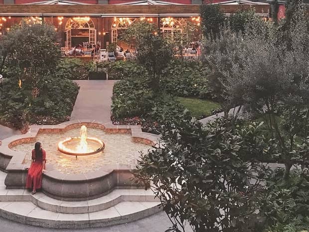 Looking down over courtyard where woman in red dress sits on fountain ledge