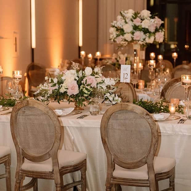 A banquet table decorated for a wedding with white linens, pink and white floral arrangements, greenery and tea light candles in glasses