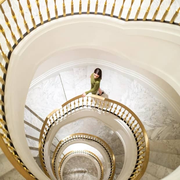 A woman walking down marble spiral stairs.