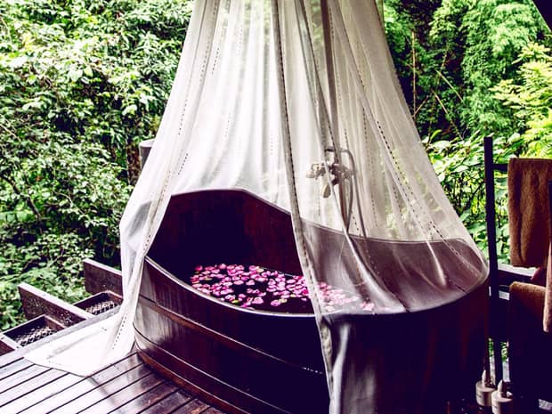 Outdoor spa tub filled with purple flower petals under white canopy on patio