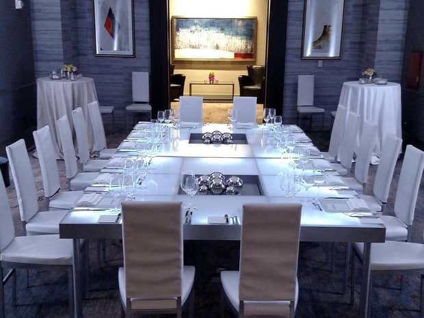 White boardroom meeting table, chairs in dimly-lit event space 