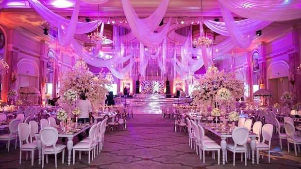 Wedding banquet with white dining tables, fabric strung across ceiling, purple lights 