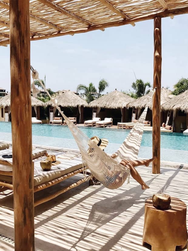 Woman in sun hat with legs dangling over side of hammock on patio, beside swimming pool