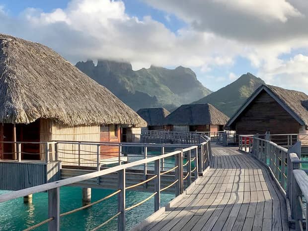 Curved bridge connects overwater bungalow suites with thatched roofs
