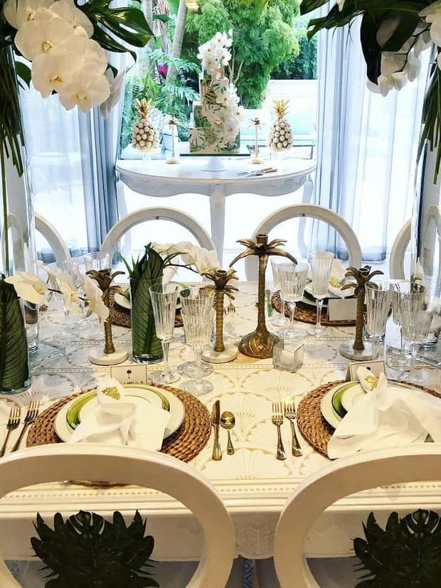 Elegant banquet dining table with white orchids, tropical flowers, brass palm candelabras 