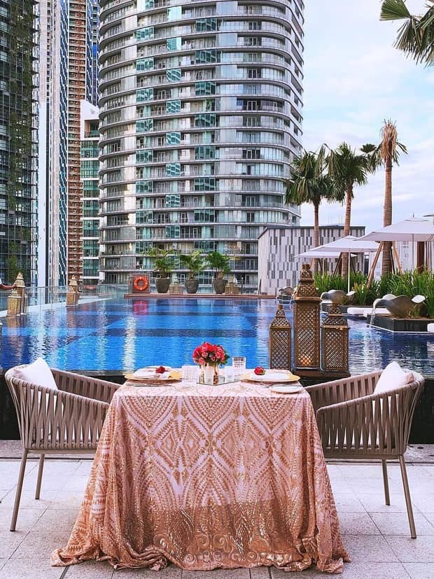 A poolside dining table with two chairs decorated with linens and flowers