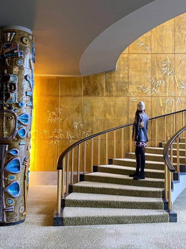 A woman looking at a stone wall while walking up curved stairs.