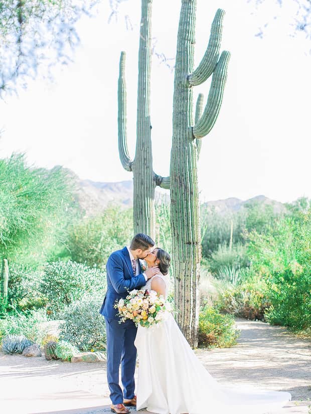 Bride and groom kiss under tall cactus plants in garden