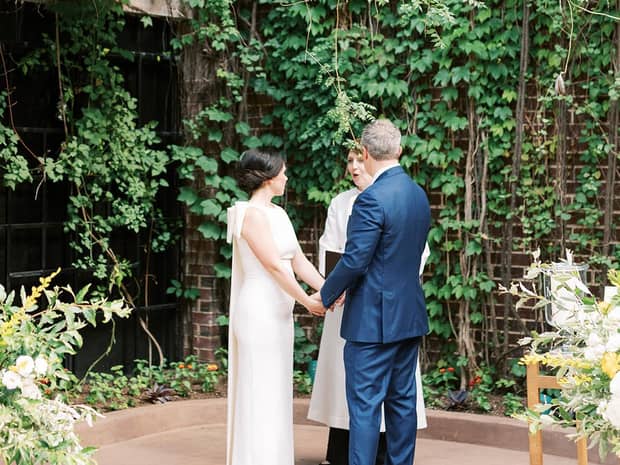 Bride and groom hold hands at garden patio wedding ceremony