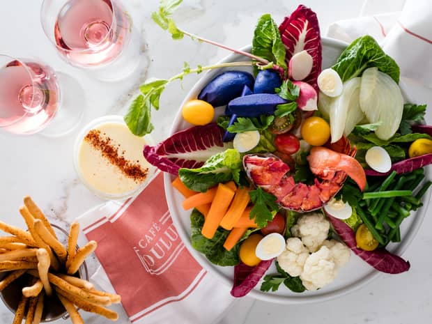 Aerial view of salad piled high with fresh lobster, carrots, cauliflower, tomato, lettuce, pink Champagne in glasses