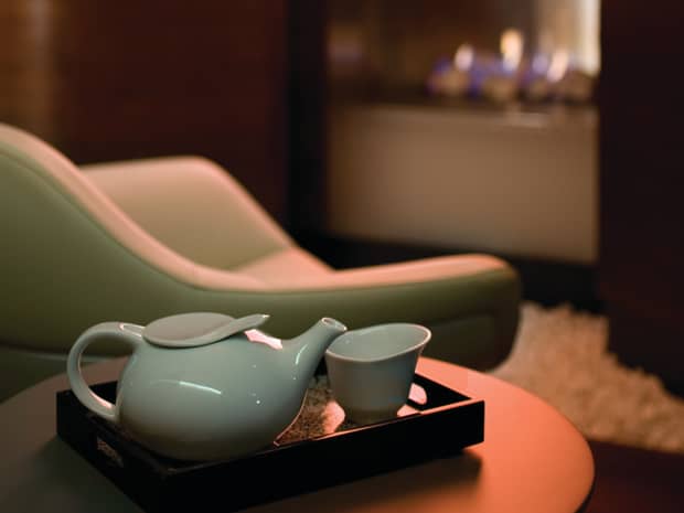 Modern white tea pot, cup on tray by leather chair, fireplace in background
