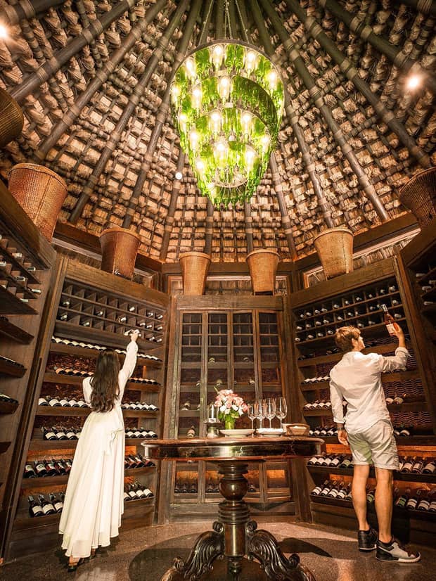 Man and woman select bottles of wine from walls of dome shaped cellar under chandelier