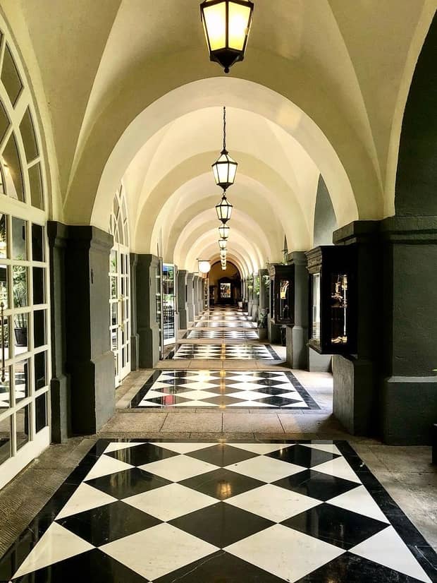 Black and white marble floors down long hallway under arched ceilings, lanterns
