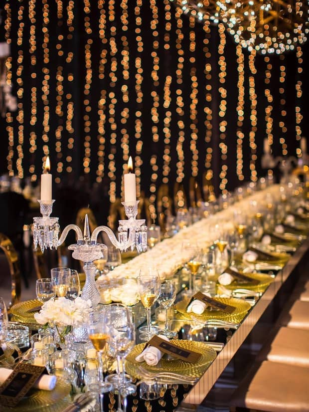 Long wedding banquet table with crystal candelabra, wall with string lights 