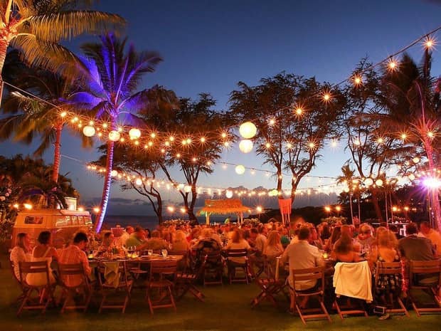 People gathered around tables at outdoor wedding reception under string lights at night