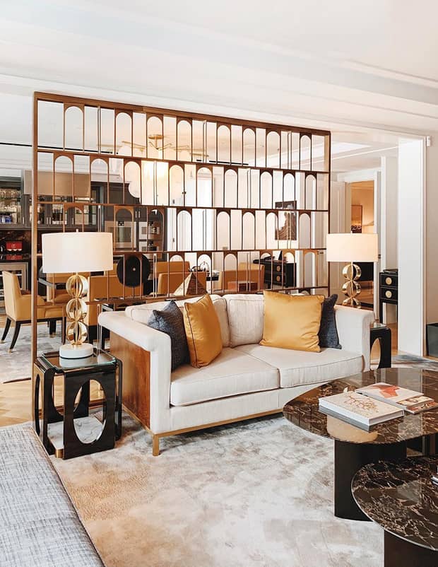 Elegant living area featuring a cosy sofa with gold accent pillows, stylish lamps, a chic coffee table and a modern room divider with arch motifs