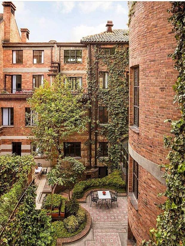 Looking down at courtyard patio surrounded by brick building, windows, green trees, shrubs 