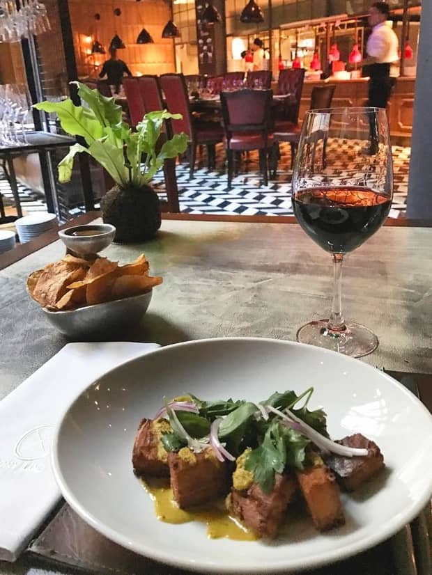 Meat dish with lettuce, sliced red onion, glass of red wine and bowl of crisps on restaurant table