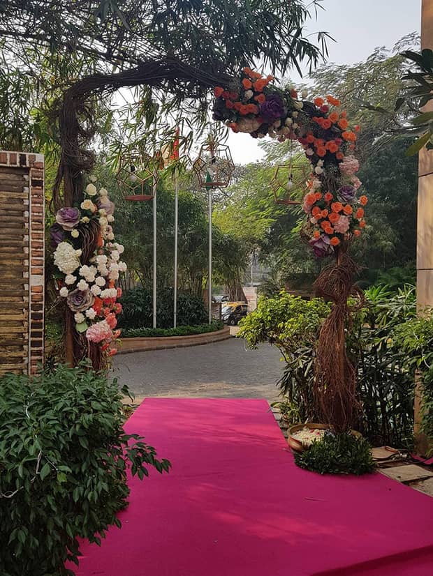 Rustic wedding archway with colourful flowers, near brick road and courtyard 