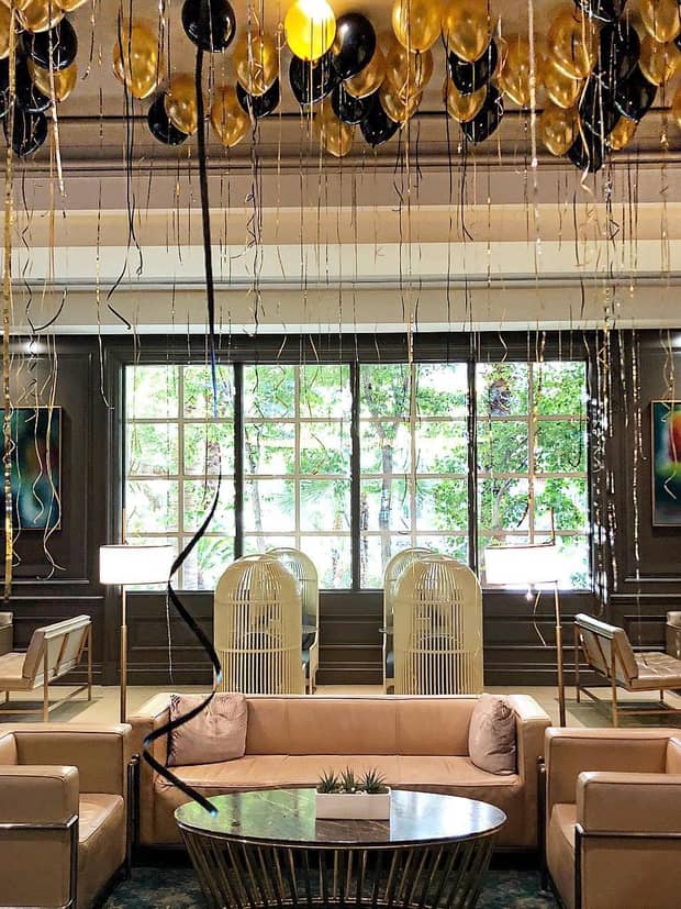 Gold and black balloons with ribbons along ceiling over seating area