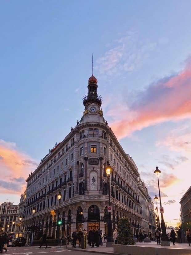 A large stone building during sunset with people standing outside of it.