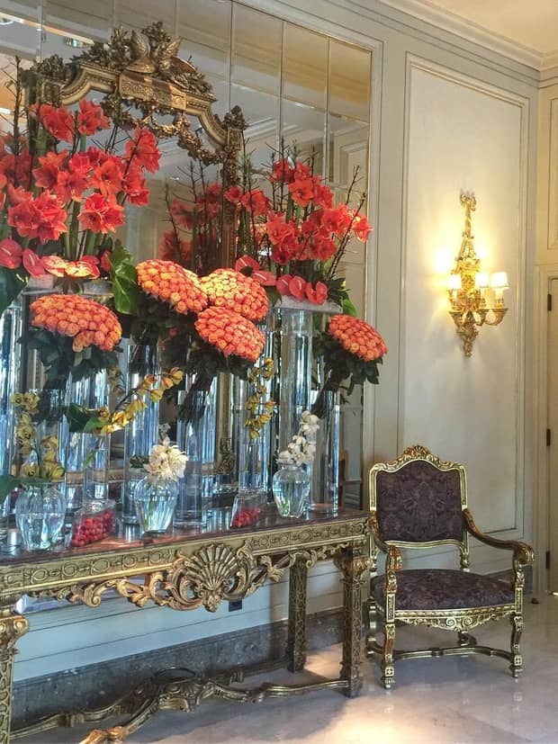 Red and orange floral displays on antique style gold console table, chair under lantern