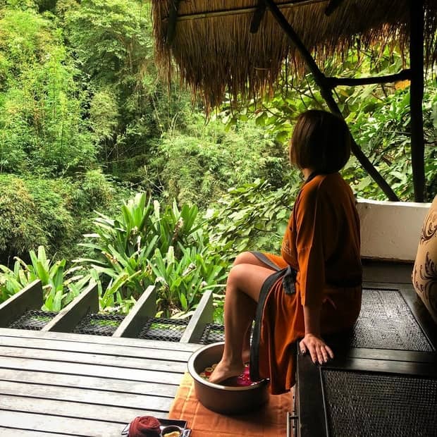 Woman in silk robe sits on wood steps, feet in bowl of water 