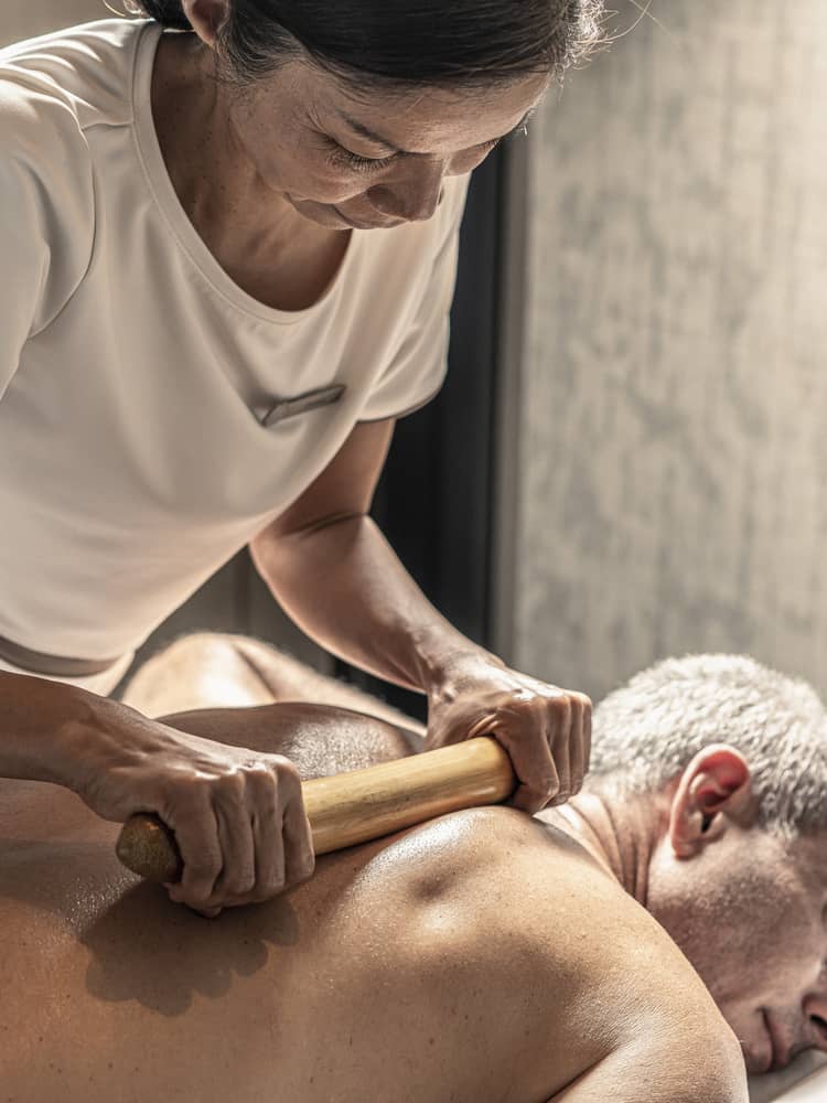Massage therapist performs a bamboo massage on male guest