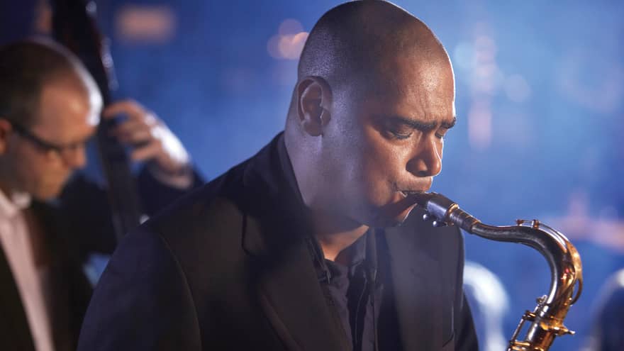A close up of a man with his eyes closed, playing a saxaphone at a Jazz club in Ten Trinity 
