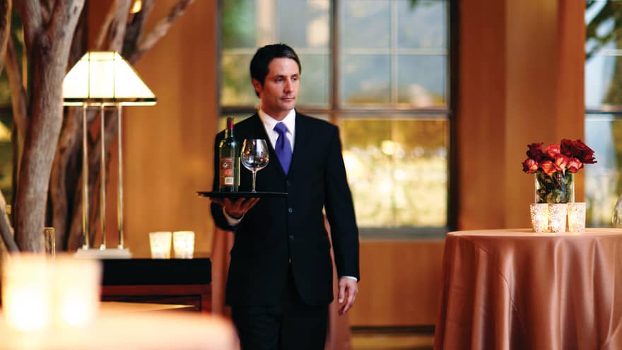 Hotel staff carries tray with wine across event room