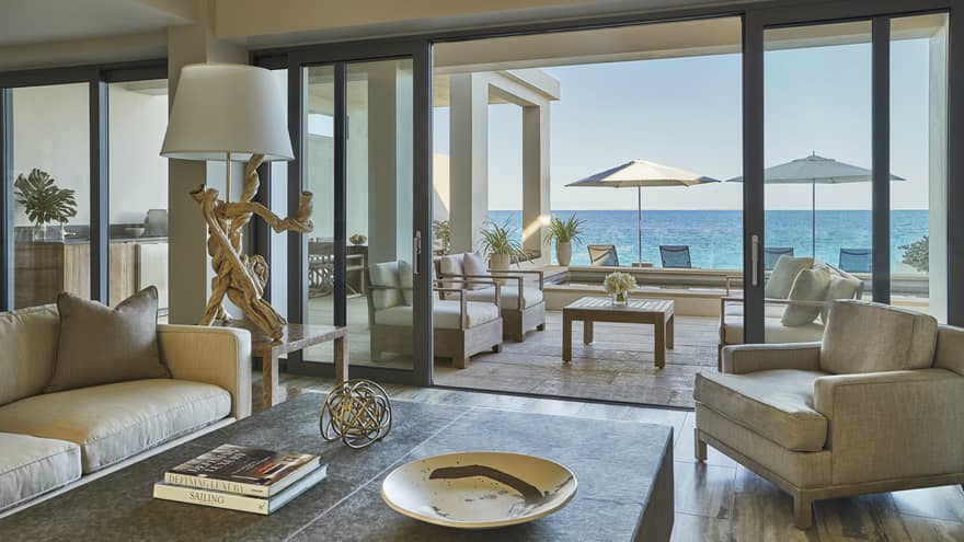 View from inside to indoor-outdoor living rooms with sofas, chairs, patio umbrellas and ocean in background