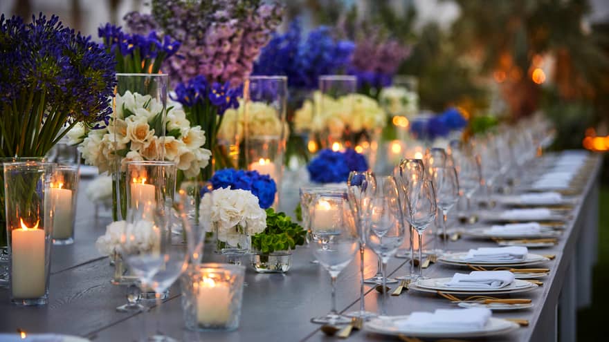 Close-up of banquet dining table with glowing candles, white and blue flowers