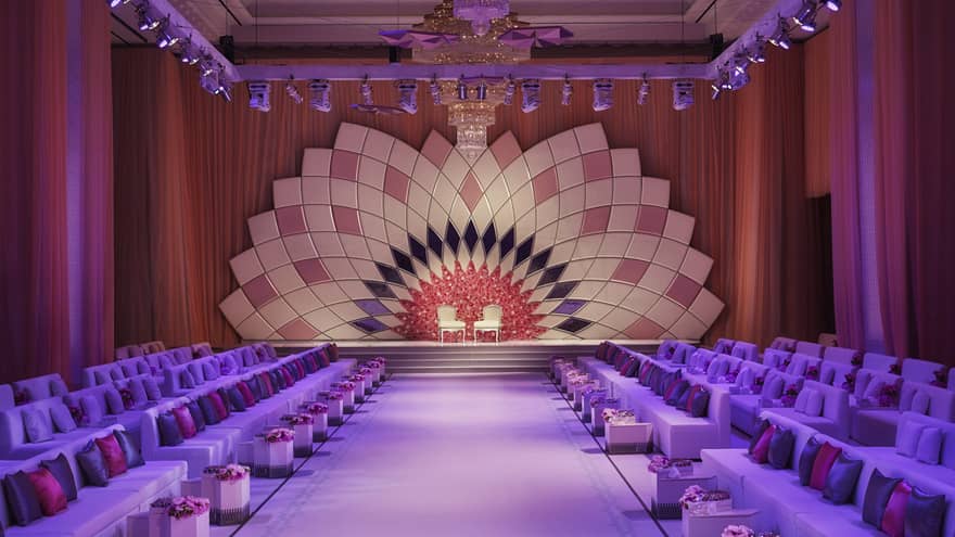 Large event room with stage and two chairs, rows of lounge sofas along runway