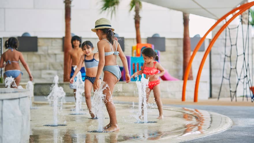 Children in swimsuits run and play on outdoor splash pad