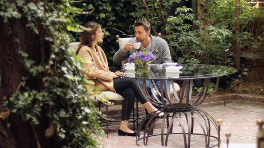 Couple drinks coffee at small glass patio table in garden