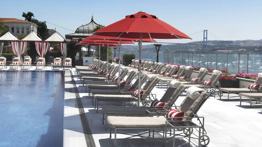 Rows of lounge chairs and red patio umbrellas on outdoor swimming pool deck