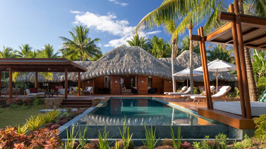 Private pool in a villa, with white sun chairs and a thatched-roof patio