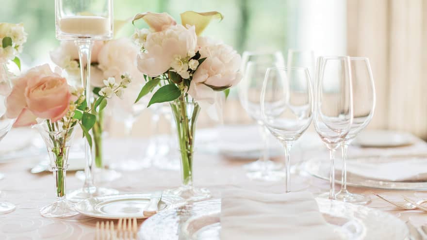 Dining table place setting with glassware, small vases with pink roses
