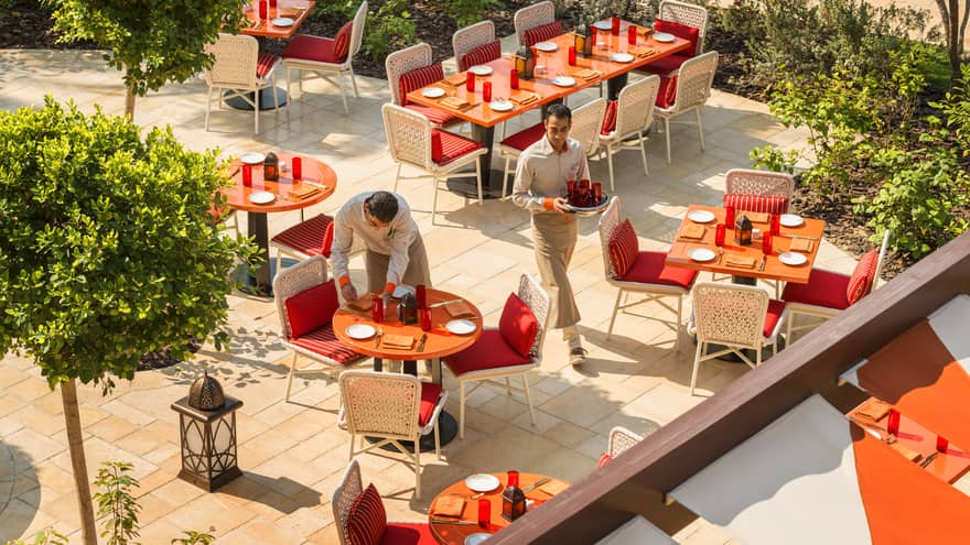 An aerial view of SUQ Terrace, with its round orange tables, red and white chairs, groomed trees and waiters