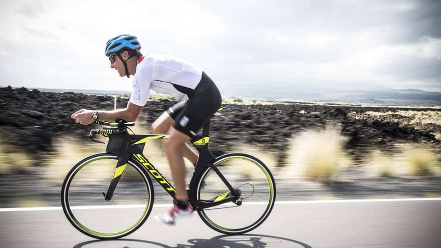 Man wearing cycling gear, helmet rides bicycle down road during triathlon
