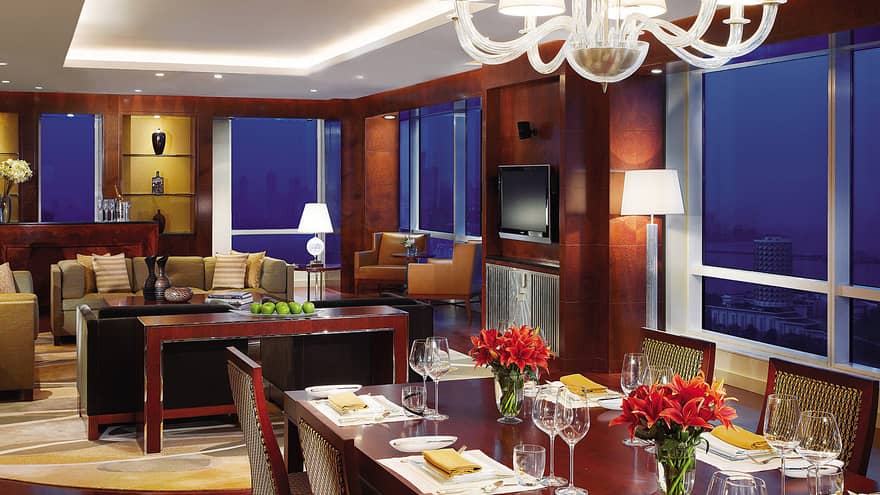 Presidential Suite long dining table under chandelier, seating area, corner windows at night