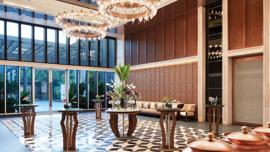 Spacious foyer with Art Deco style tile floors, cocktail tables under tall windows, round lantern chandeliers 