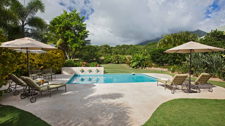 Small residence plunge pool by green lawn, plush lounge chairs on deck