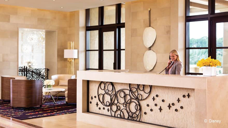 Woman answers phone at large reception desk by seating area with brown bucket chairs