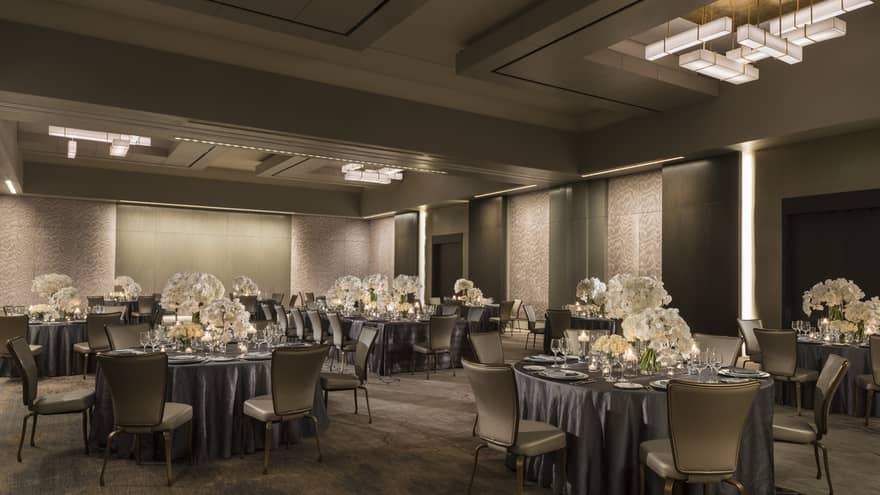 Dimly lit ballroom banquet with round tables, large white flower centrepieces