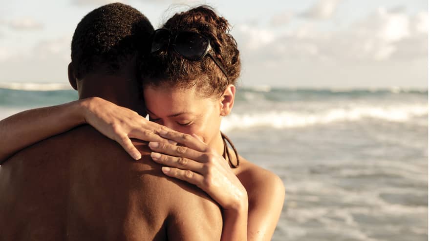 Couple wearing swimsuits embrace on beach by waves