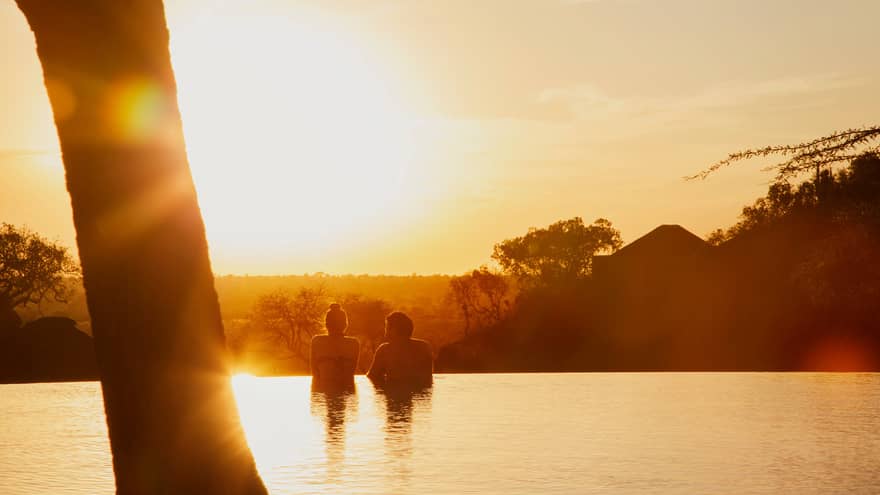Silhouettes of couple wading in infinity swimming pool at sunset