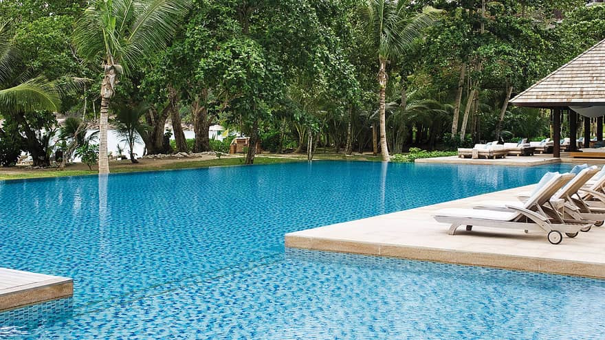 Row of white pool lounge chairs along side of swimming pools, palm trees in background
