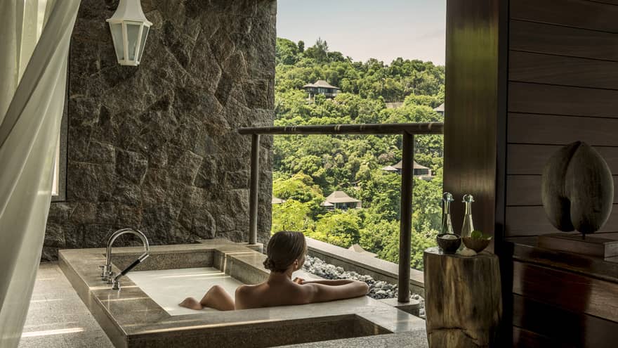 Back of woman sitting in rectangular hot tub, looking out open wall at mountain